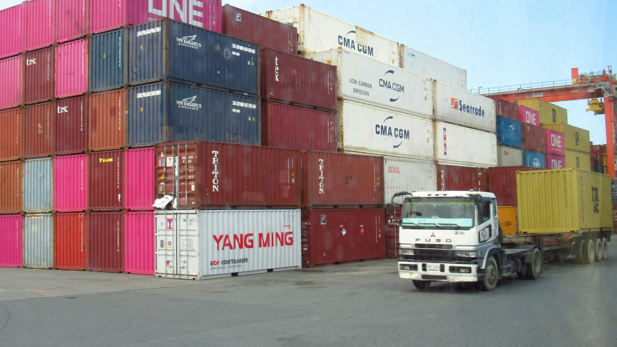 Freight truck moving beside stacked shipping containers